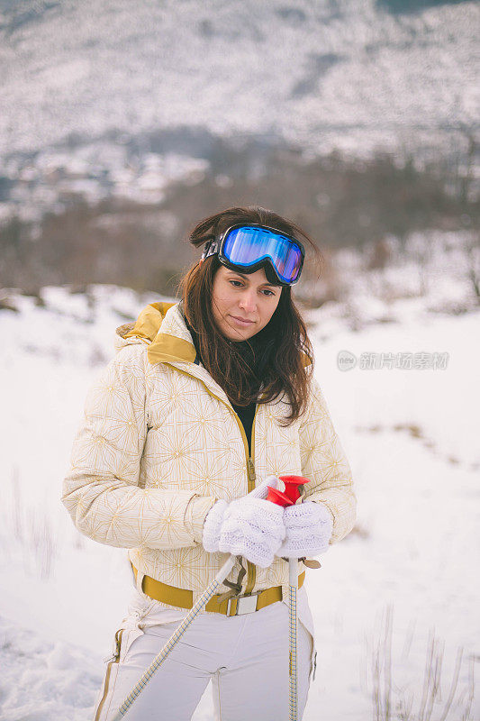 近景美丽的年轻女子在冬天的衣服站在一边，手拿木棍的背景雪山