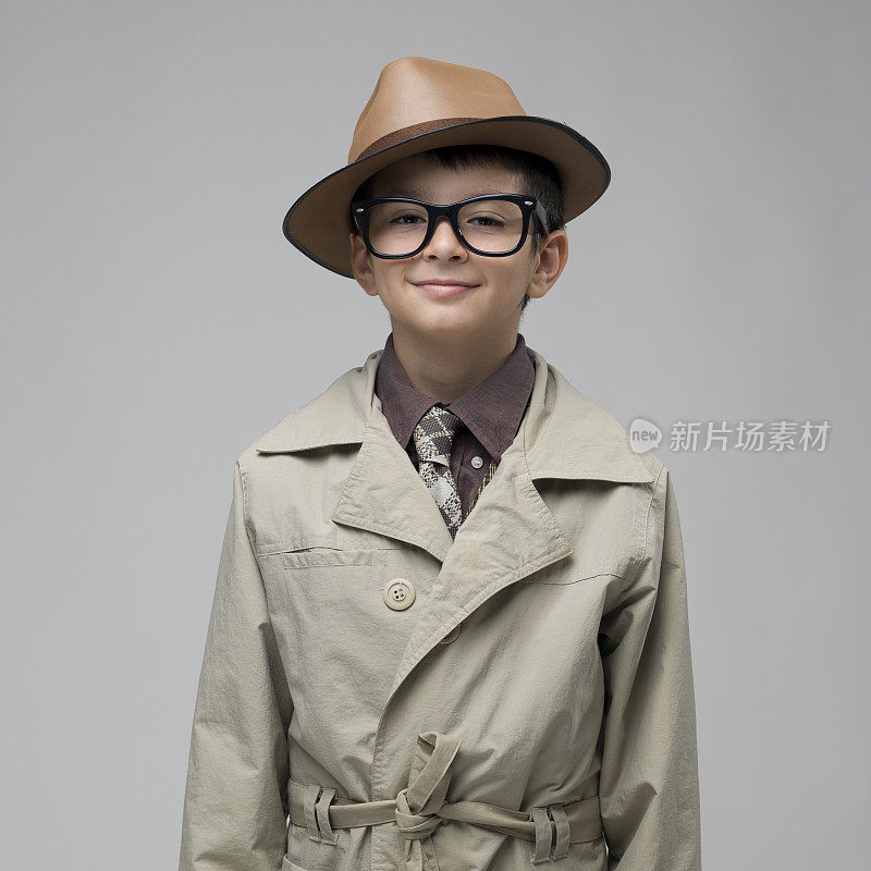 穿着风衣戴着眼镜的男孩在灰色背景下微笑。