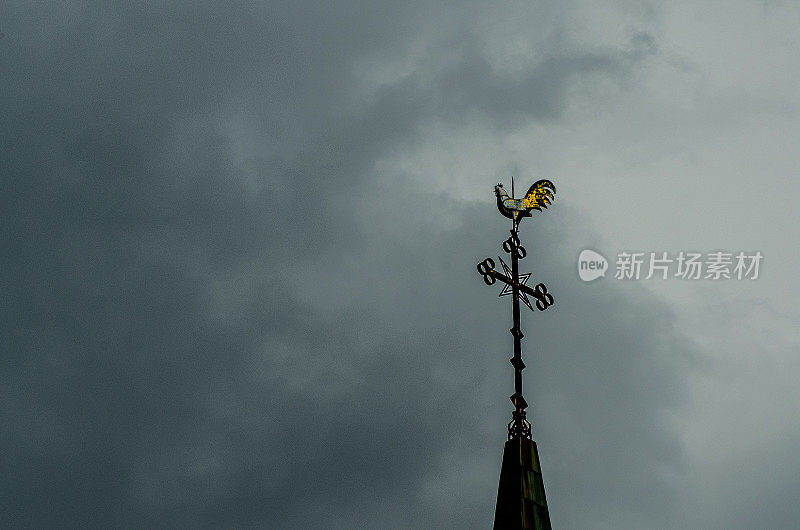 公鸡风向标在教堂的尖顶上，阴沉的暴风雨天空