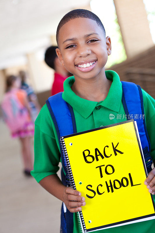 快乐的小男孩摆着“回学校”的“笔记本”牌子