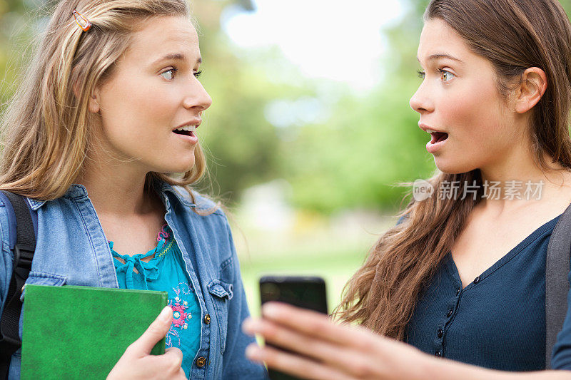 两名女学生在看智能手机屏幕时感到惊讶