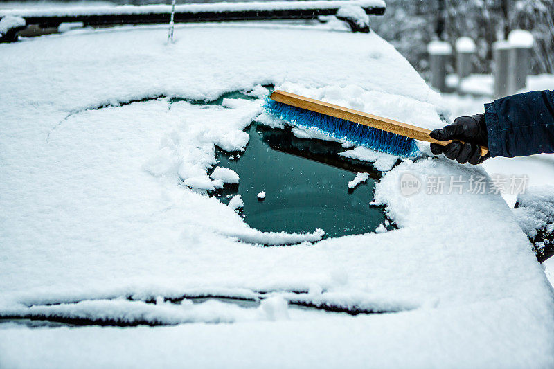 用扫帚扫挡风玻璃上的雪的人