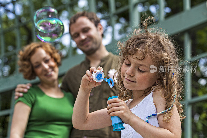 可爱的小女孩吹泡泡与妈妈和爸爸