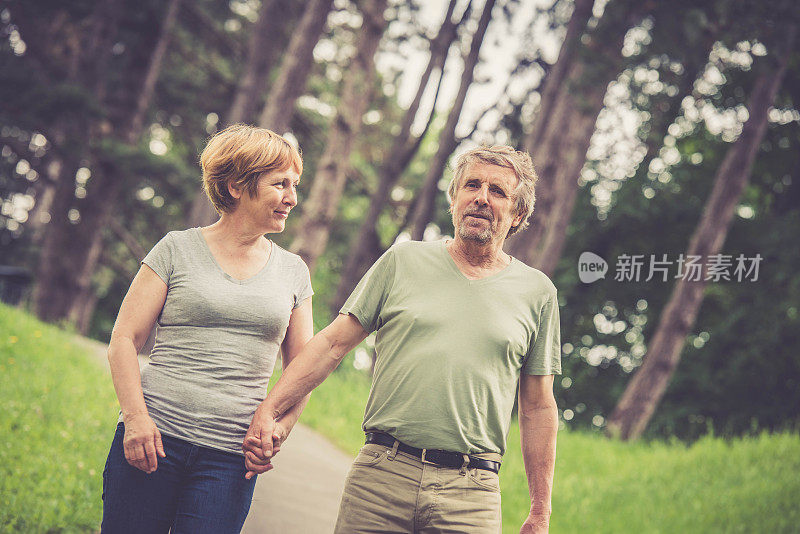 一对老年白人夫妇手牵着手在户外散步