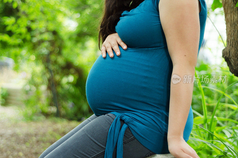 孕妇的腹部，手放在肚子上。