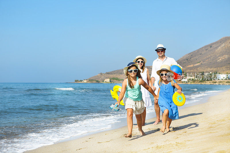 幸福的年轻的家庭在日落时在海滩上跑步。家庭旅游的概念