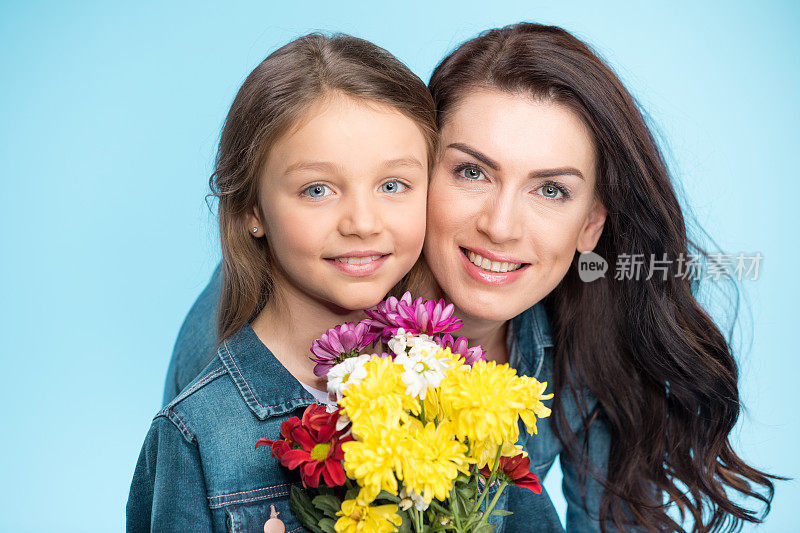快乐的母亲和女儿拥抱和捧着鲜花在蓝色工作室，母亲节快乐
