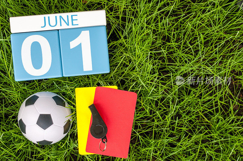 6月1日。图片6月1日木制彩色日历上的绿色草地背景与足球装备。第一个夏天