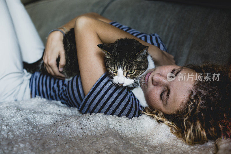 一个年轻的女人躺着，怀里抱着她的猫