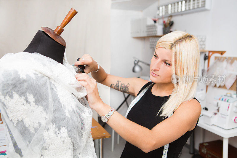 年轻的女时装设计师在她的工作室工作服装上的人体模型。