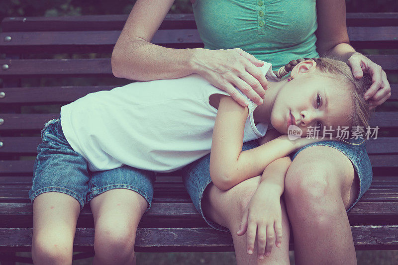 悲伤的母亲和女儿坐在公园的长凳上