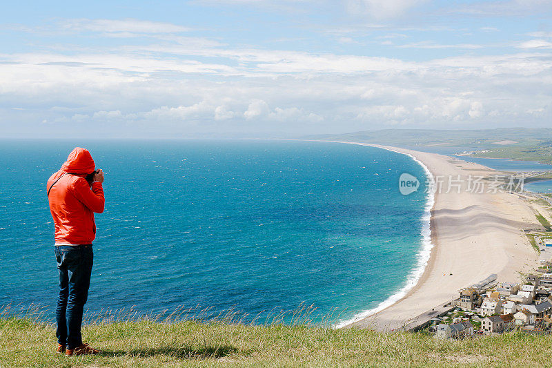 英国多塞特郡波特兰的一个观景台上，一名年轻人正在拍摄韦茅斯和海岸线的照片。