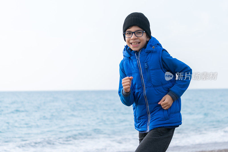 快乐男孩在一个冬日的海滩上慢跑