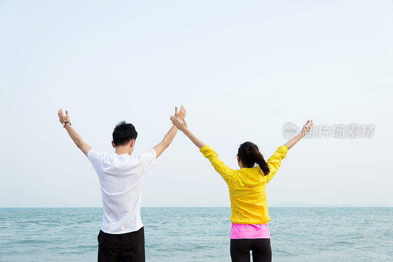 年轻夫妇在海滩上举起双手