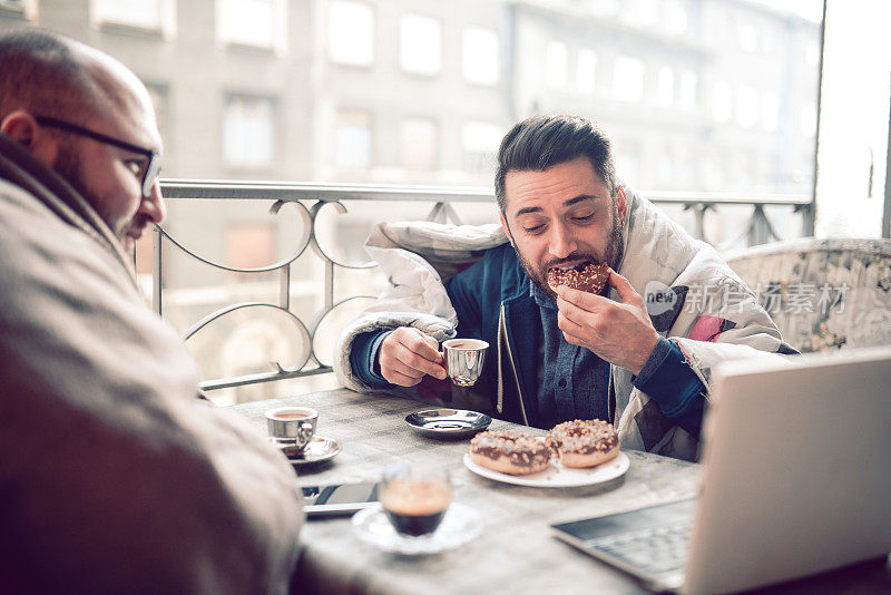 两个微笑的商人在阳台上喝咖啡吃早餐