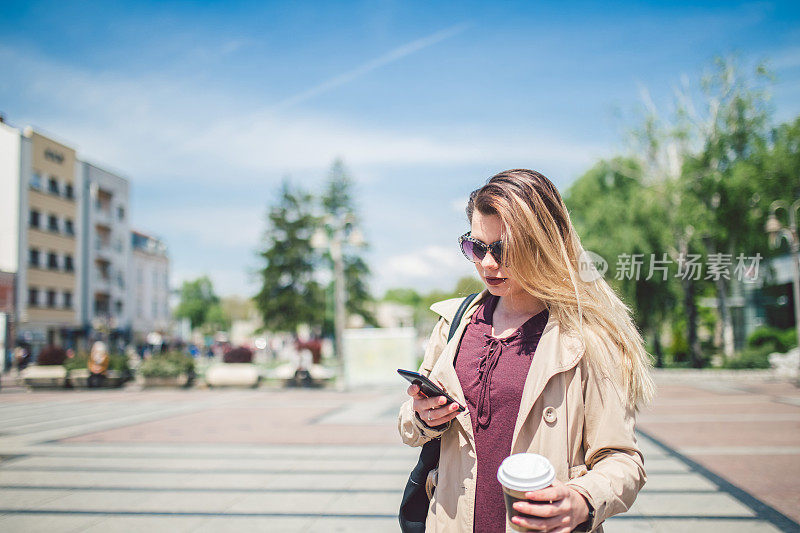 一个女人走在城市广场上玩手机。