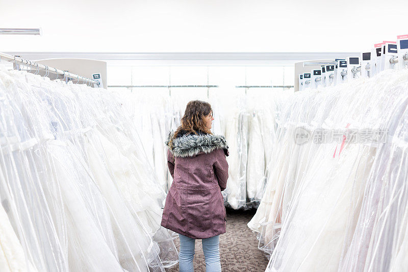 年轻女子在精品店的折扣店购买婚纱礼服，许多白色服装挂在衣架排