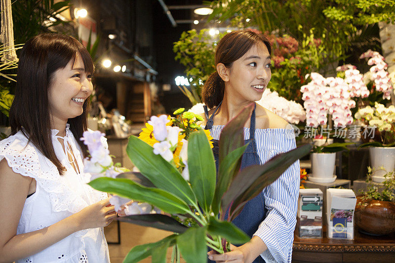 在花店里帮助一位挑选向日葵和树叶的妇女的店员。