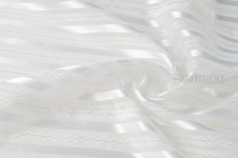 背景纹理、图案。白色的丝质织物，带有一条带。波纹白色丝绸织物的特写。柔滑优雅的金丝可作为婚礼背景。复古的风格