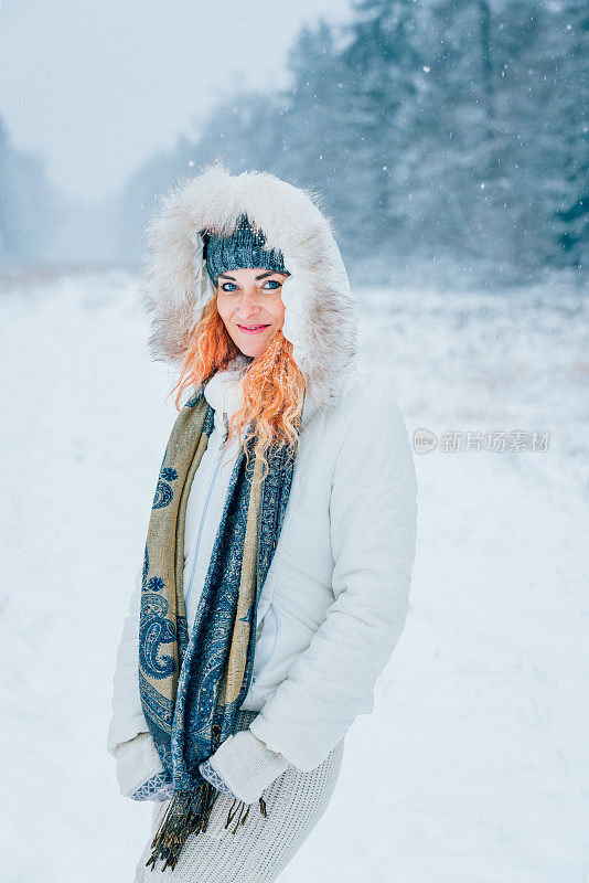 快乐的女人，在冬天森林附近的白雪皑皑的草地上