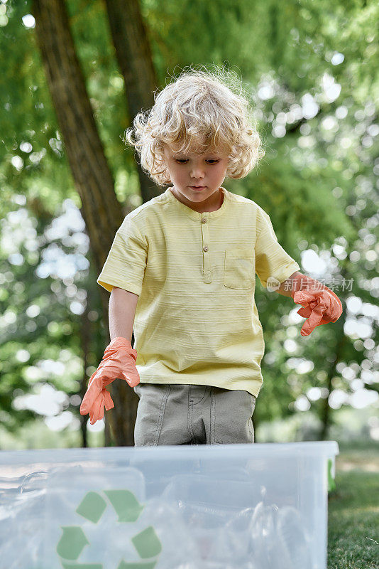 可爱的白人小男孩戴着橡胶手套在森林或公园收集塑料垃圾，回收塑料瓶