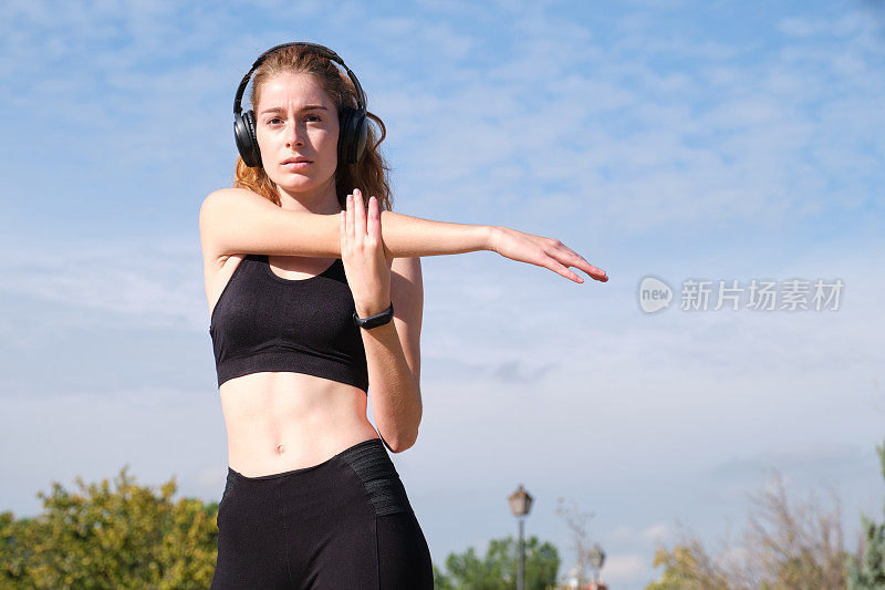 红发白人妇女戴着耳机伸直手臂。户外健身和运动。红发，白种人，女人，伸展，手臂，耳机，健身，手臂，运动，户外，人，耳机，音乐，运动员，锻炼，准备，准备，听，健康，女性