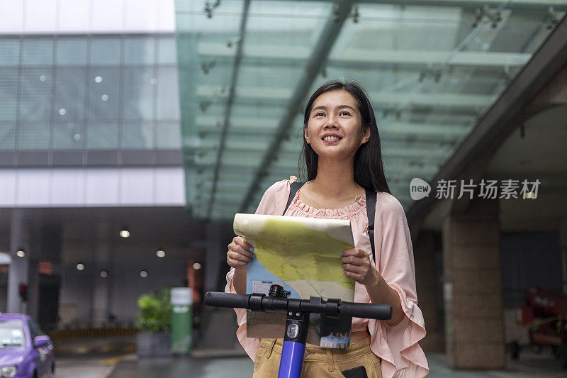 一个女人拿着地图，骑着电子滑板车在外国城市里探险