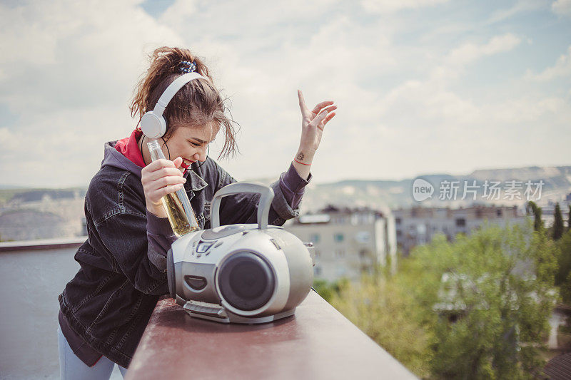 年轻女孩在建筑的屋顶上度过她的时间和享受的时刻-在建筑的屋顶上听音乐，享受自由和喝酒