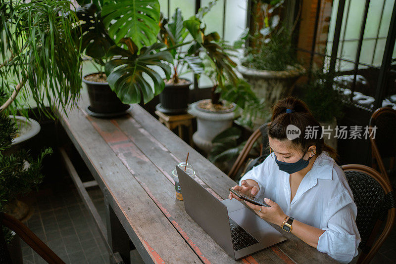 自由职业者在咖啡馆用手机和笔记本电脑戴防护口罩。