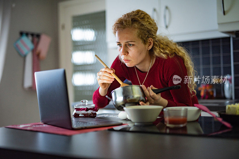 一名女子一边在家准备饼干，一边在笔记本电脑上阅读食谱