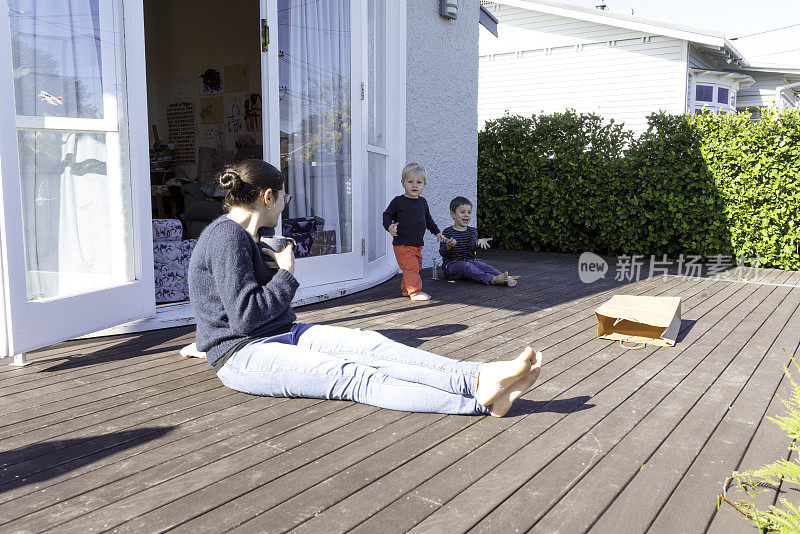 年轻的母亲和两个学前班的儿子在家里的阳光下玩耍