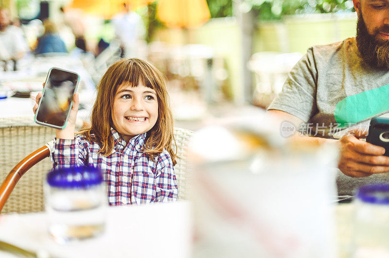 孩子在户外餐厅与家人一起使用手机，享受科技和坦诚的家庭团聚