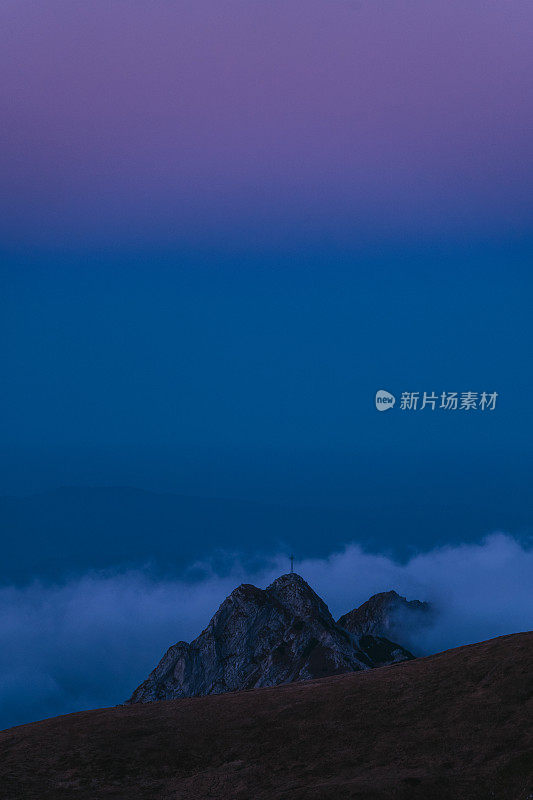 壮丽的风景与塔特拉山后日落。山峰与十字剪影对蓝色和粉红色的天空和浮云