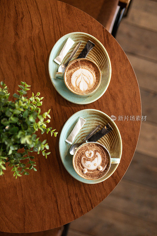 两杯带拿铁图案的咖啡放在咖啡馆的木桌上