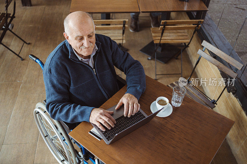 快乐的残疾老人在咖啡厅用笔记本电脑