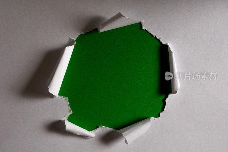 在白硬纸板上撕开一个洞。白色撕裂纸洞与绿色的背景