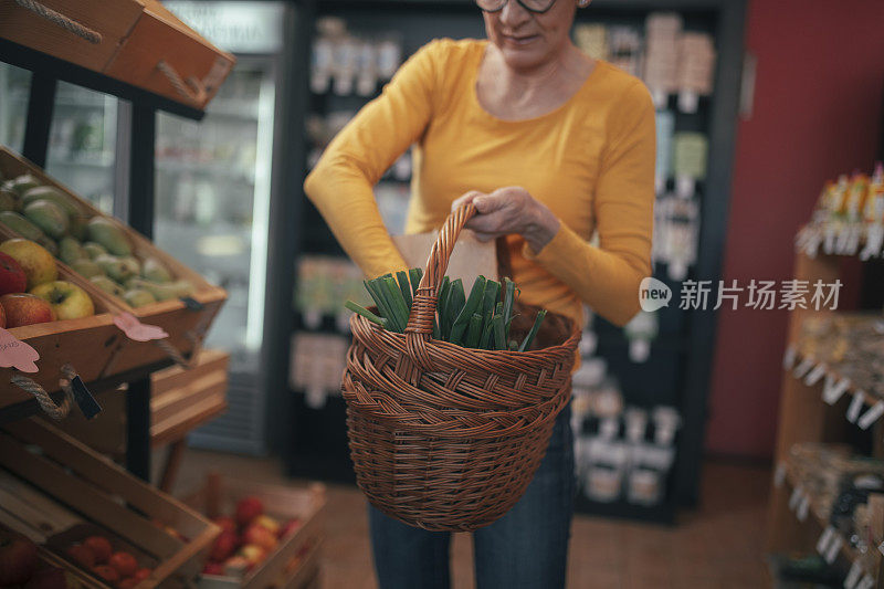 在一家有机食品店，一位不知名的妇女拿着一篮子新鲜蔬菜。