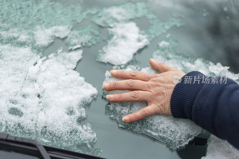 下雪后的冬天，妇女不戴手套，赤手空手清洁被雪覆盖的车窗。