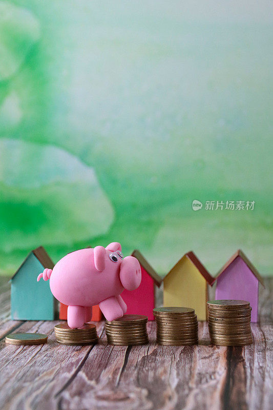 图像的彩色纸板房子后面的小猪银行爬楼梯堆叠的硬币，重点是前景，斑驳的绿色背景，复制空间，家庭财务，房地产和假日储蓄的概念