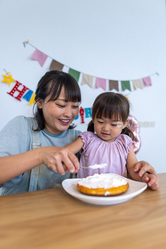 母女俩在家把奶油涂在生日蛋糕上