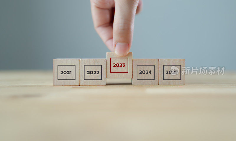 关注2023年。新年业务规划与策略。性能和亮点的概念。拿着灰色背景上编号为2023的木质立方体。年初概念。2023年旗帜。