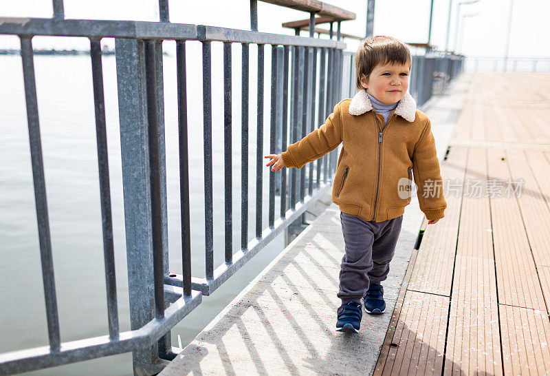 一个穿着暖和衣服的男孩沿着黑海附近有栅栏的码头走着
