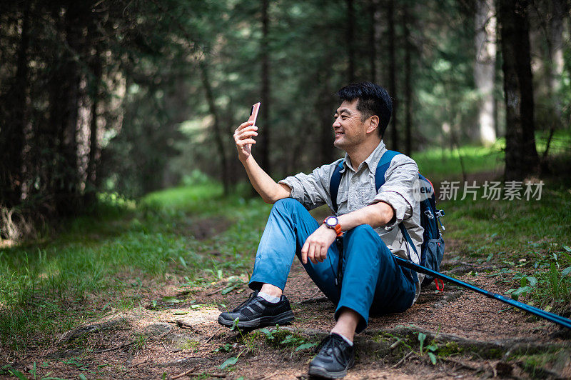 亚洲中年男子在森林徒步旅行时用智能手机拍摄美丽的风景