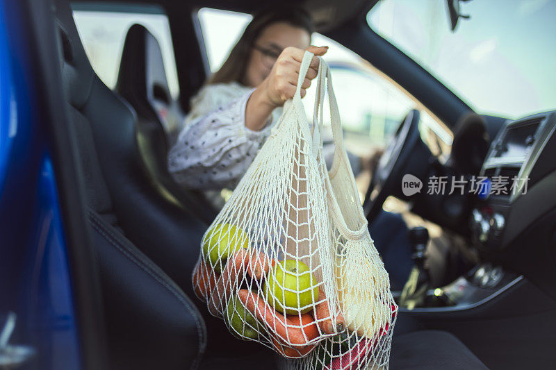 一个女人手里拿着一个装着水果和蔬菜的网眼袋的特写