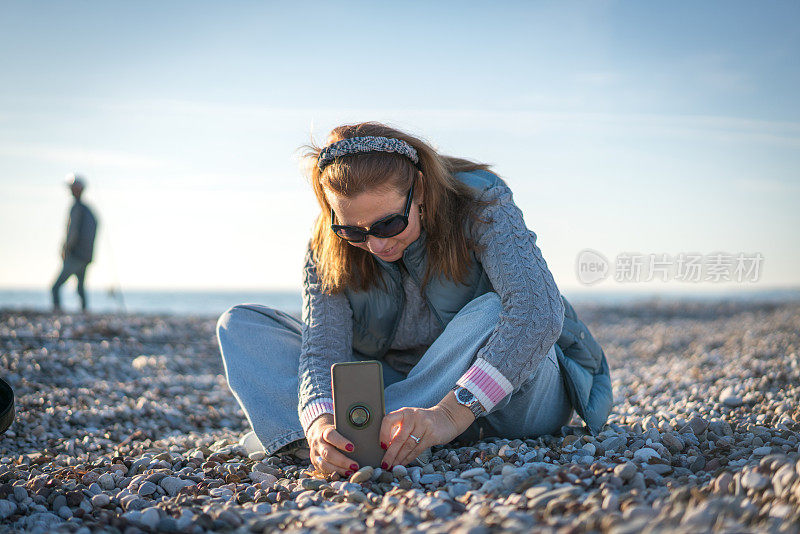 成熟美丽的白人女子在海滩上使用电话。