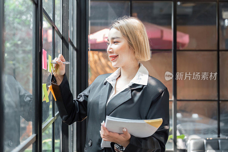 小公司的亚洲女企业家在分析制定商业战略时，在办公室的玻璃墙上贴了一张粘性便签。