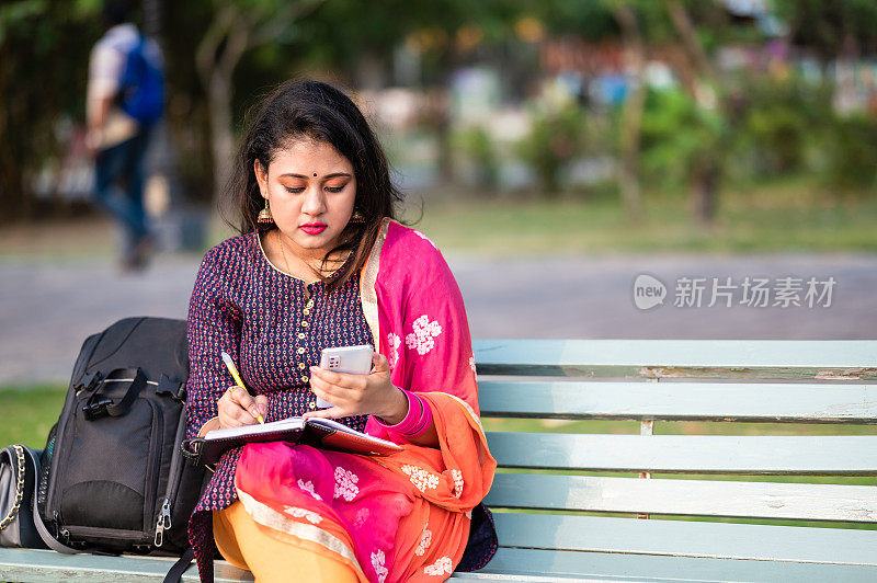 有吸引力的年轻白人女子坐在木凳上，在公园写日记。