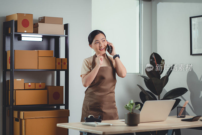 亚洲女性在线卖家在家里办公室用智能手机打电话给客户确认订单。