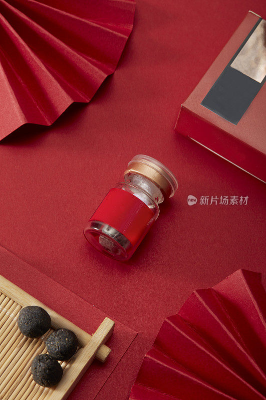 中国风红色的背景和红色的折扇和红色的金盒子和三个中药药丸放在一个竹篮和一个红色的药丸瓶