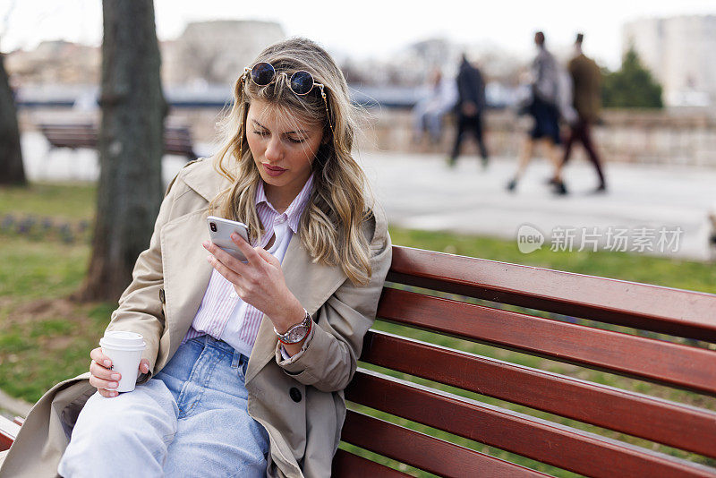 年轻女子一边在公园长椅上放松，一边喝着外卖咖啡